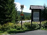 Rozcestník a infopanel u silničky nad přehradou Souš. V pozadí vrchol tisícovky Černý vrch.