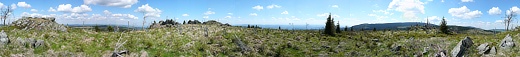 Kruhové panorama ze středu vrcholové plošiny Meluzíny. Zleva: zcela vpopředí jedna z několika skalek na vrcholové plošině Meluzíny (tato z geodetickým bodem), před vzdálenou skupinou větrných elektráren charakteritická zalesněná "čepice" Vysoké seče, blíž