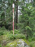Tyč a nenápadný plochý kovový geodetický bod na vrcholové skalce Tetřeva. Nejvyšší místo je ale přibližně 6 m od tyče severně.