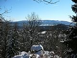 Výhled ze skalky u geodetického bodu na Žlebském kopci. Na horizontu hraniční hřeben s Plechým, Trojmeznou, Třístoličníkem a dalšími tisícovkami, blíže zalesněná Kapraď.